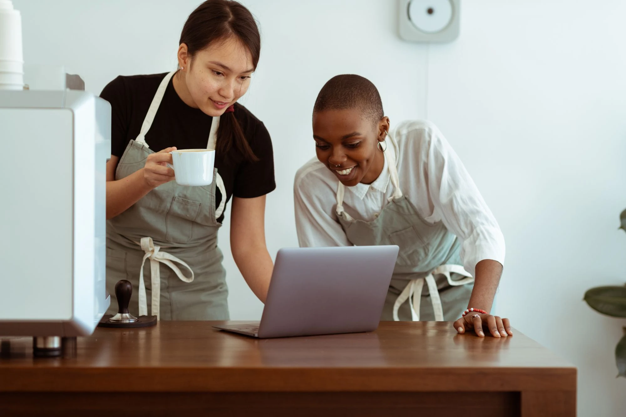 Two café colleagues smiling as they look at a laptop together.